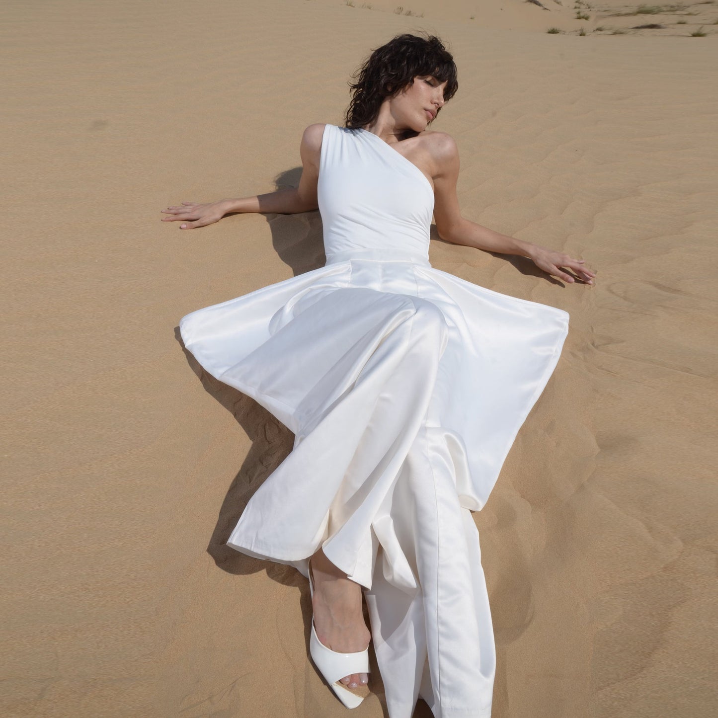	A woman in Nayades the Label's Coco de Terre Trousers White laying in the sand.